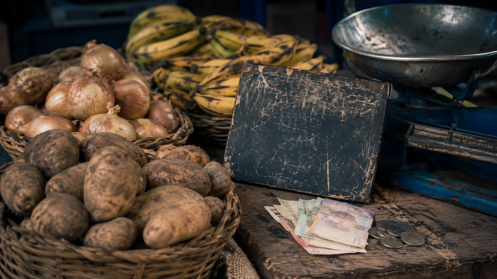 Puesto de una plaza de mercado colombiana con papas, cebollas y billetes de peso sobre el mostrador, que ilustra el efecto de la inflación en la canasta familiar en Colombia