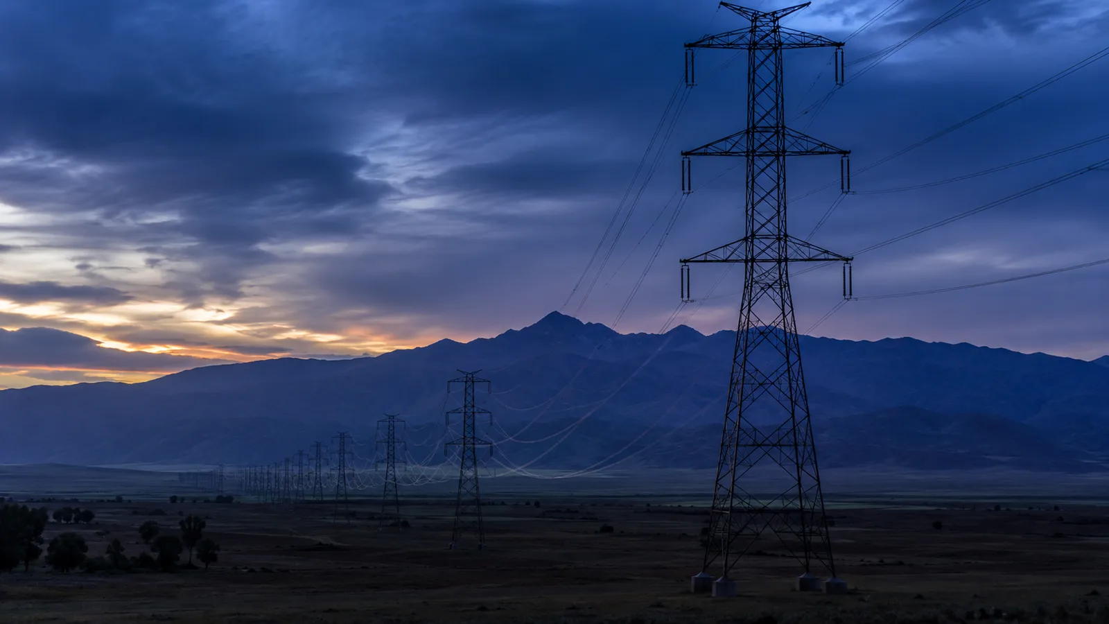 Torres de transmisión eléctrica de alta tensión cruzando un paisaje andino al atardecer, imagen del monopolio natural de las redes de servicios públicos