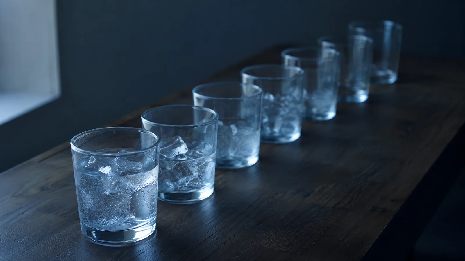 Fila de vasos idénticos de agua con hielo sobre una mesa, cada uno menos apetecible que el anterior, imagen que ilustra la utilidad marginal decreciente.