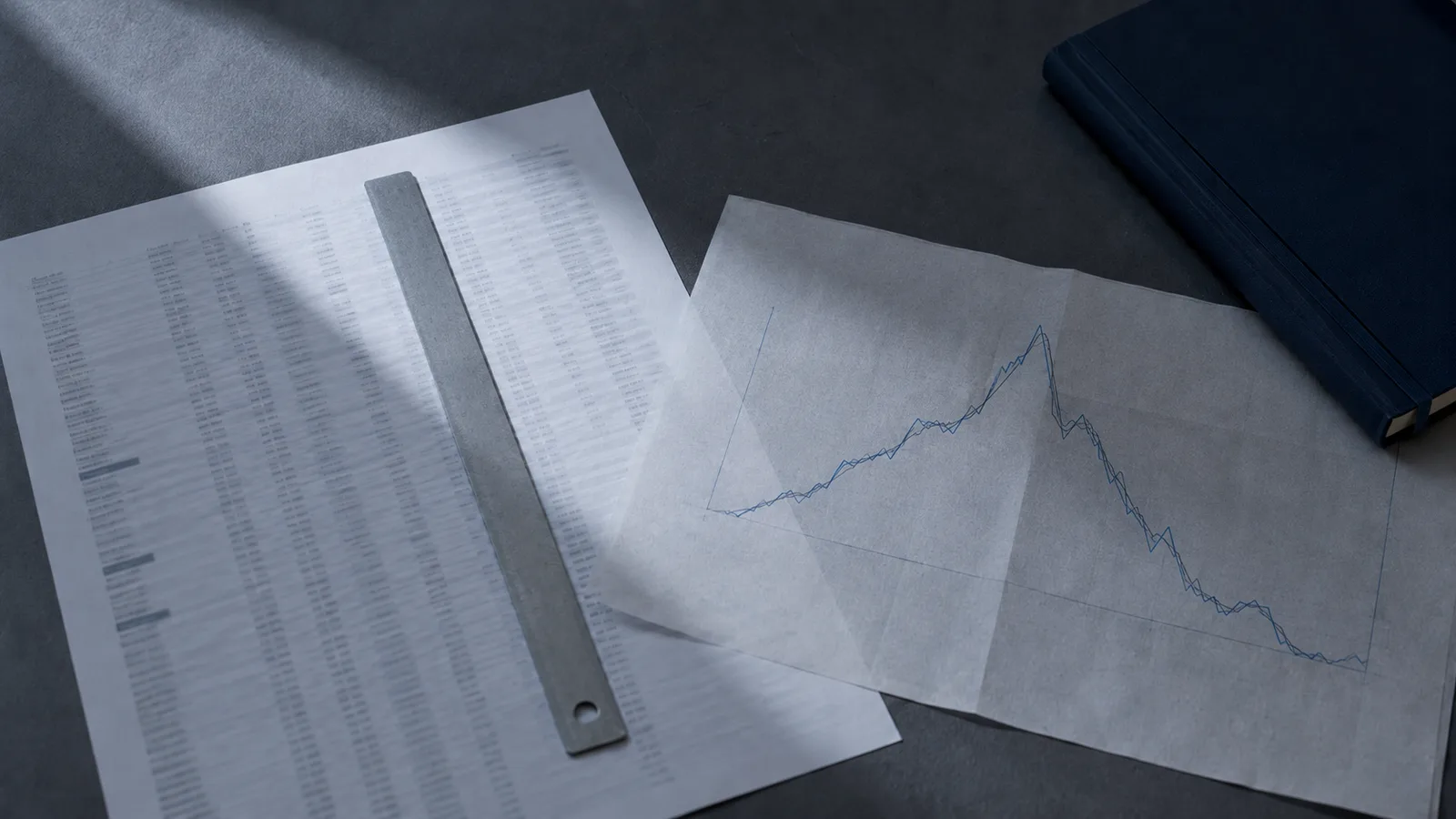 Escritorio con una tabla impresa de componentes de un índice bursátil y una regla de acero sobre un gráfico, iluminación fría azulada, concepto de fondos indexados