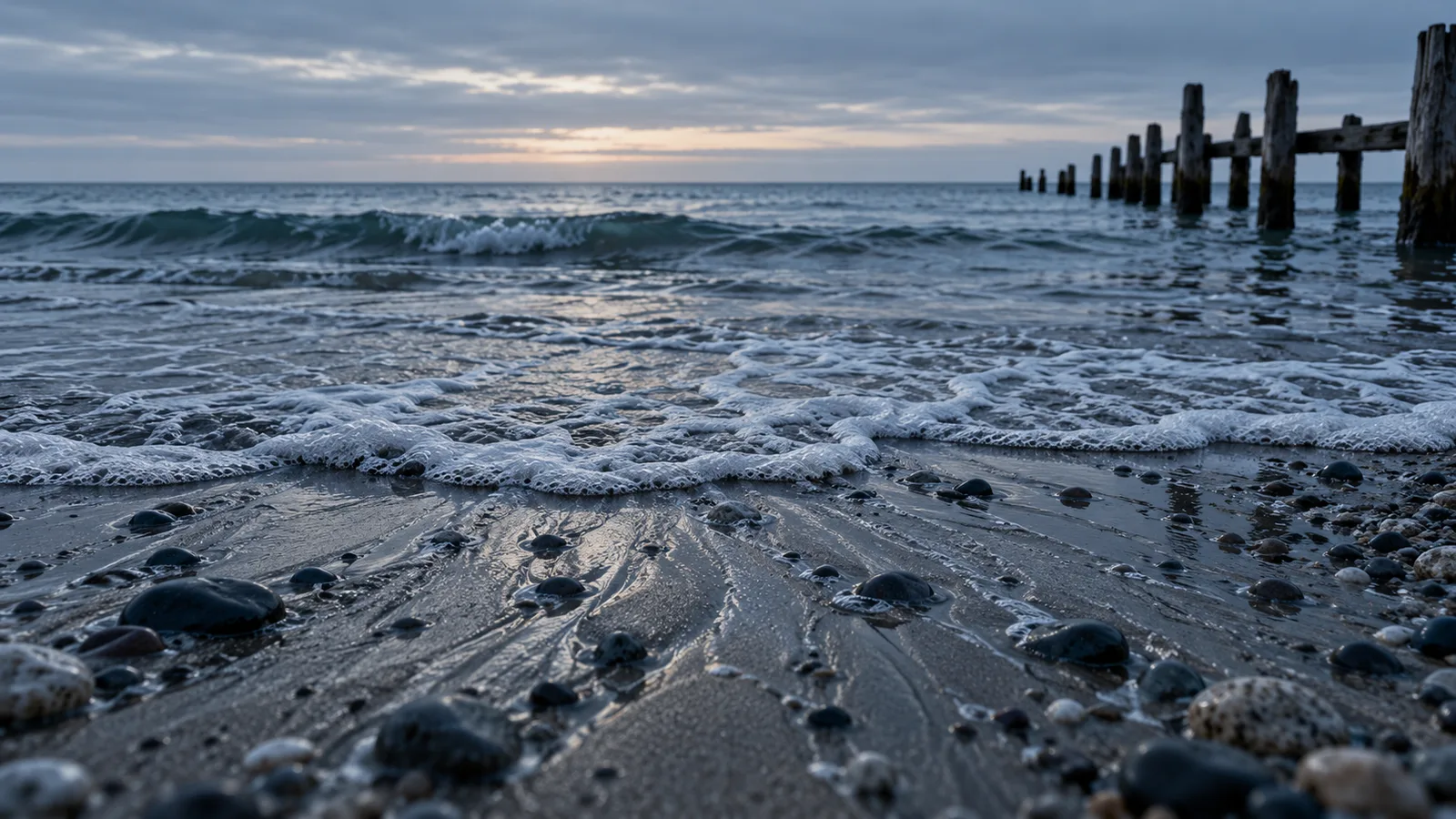 Resaca de una ola que arrastra arena de vuelta al mar en una playa al amanecer: imagen del efecto de arrastre de la causación circular acumulativa de Gunnar Myrdal